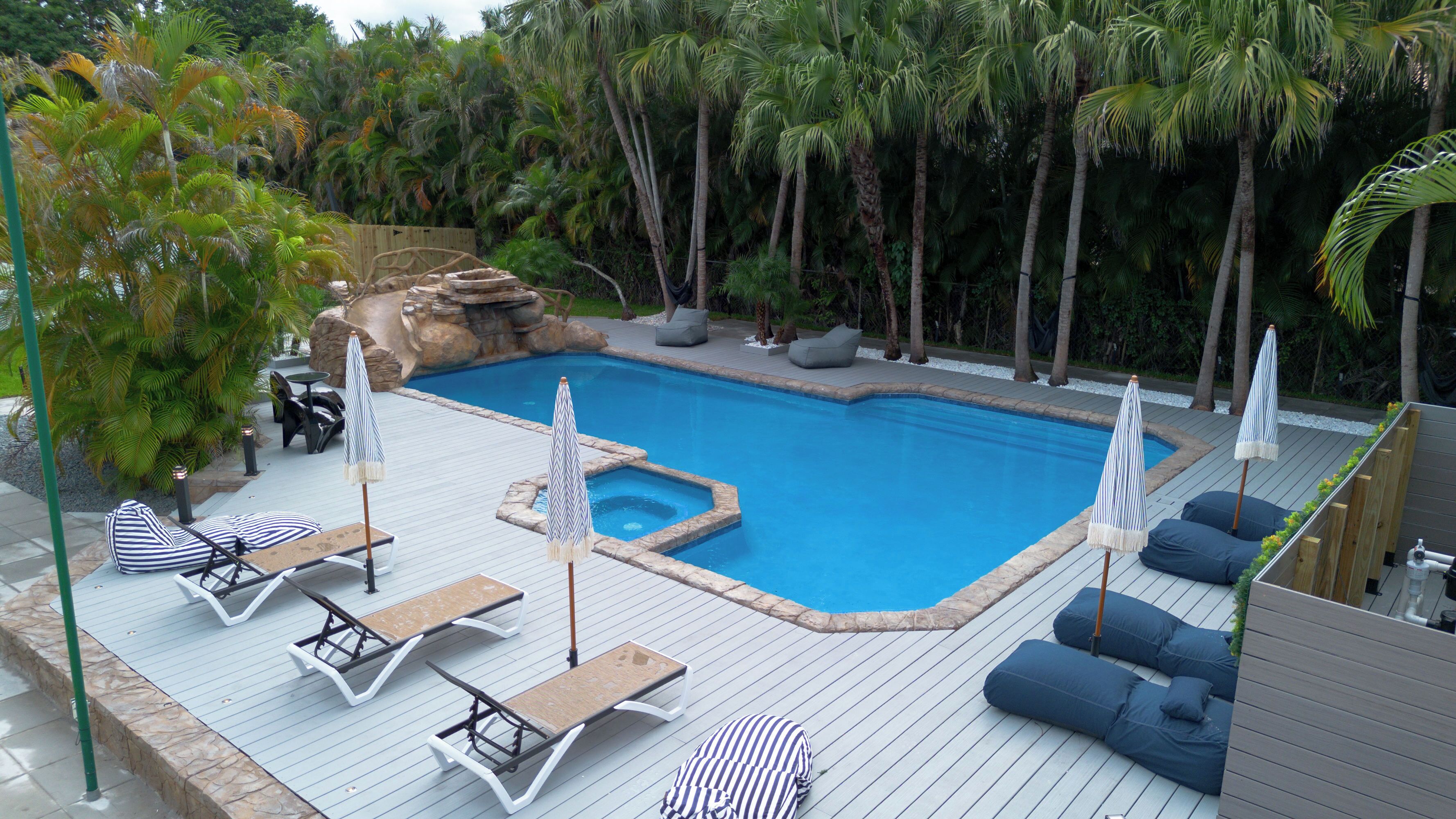 A swimming pool with lounge chairs and umbrellas, surrounded by palm trees.