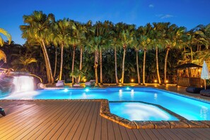 Una piscina con muelle de madera, palmeras y una cascada.