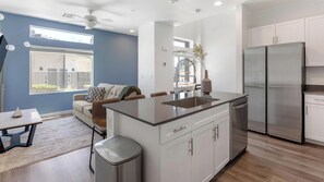 A modern kitchen with a central island, stainless steel appliances, and a dining area with a sofa and table. - Landing | Stylish 2BD, Gym (North Las Vegas)