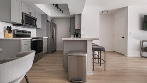 Una cocina moderna con armarios grises, electrodomésticos de acero inoxidable, una isla central y un taburete de bar.