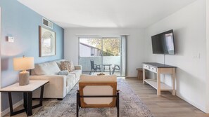 Een moderne woonkamer met een bank, een salontafel, een televisie en een balkon met tuinmeubilair.