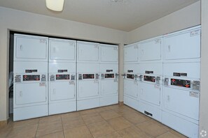 A laundry facility with multiple rows of stacked washing machines and dryers, each with control panels and labels. - Landing | Stylish 2BD, Courtyard (Paradise)
