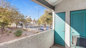 A balcony with a view of a tennis court, a teal door, and a concrete wall. - Landing | Stylish 2BD, Courtyard (Paradise)