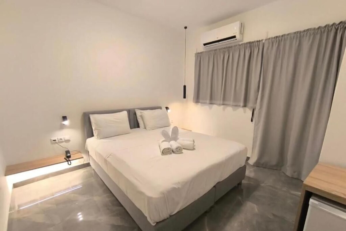 A bedroom with a bed, bedside table, lamp, air conditioning unit, and curtains.