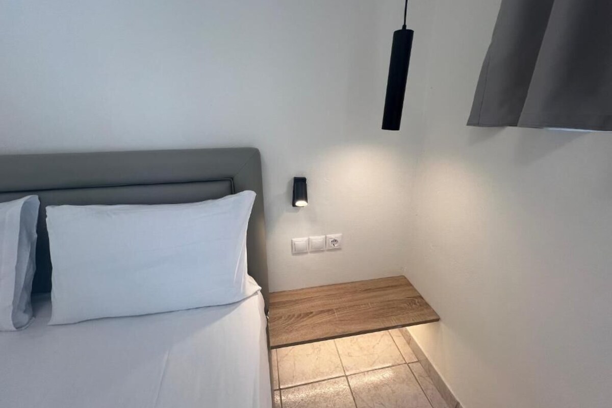 A bedroom with a bed, a bedside table, a wall-mounted light, and a curtain.