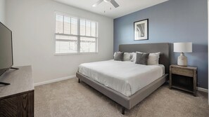 Un dormitorio con cama, mesita de noche, lámpara, ventana con persianas y ventilador de techo.