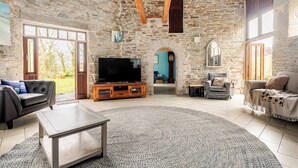 A stone-walled living room with a TV, sofas, and a fireplace. - Stunning Coastal Barn With hot tub (Falmouth)