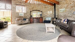 A rustic room with stone walls, a fireplace, and a large window. - Stunning Coastal Barn With hot tub (Falmouth)