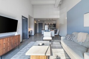 Un salon moderne avec un téléviseur à écran plat, un canapé, une table basse et un coin repas à l’arrière-plan.