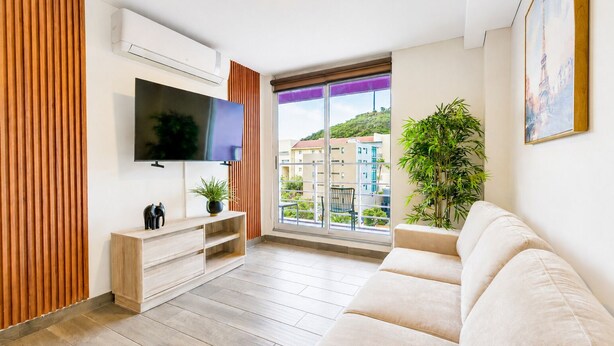 Un salon moderne doté d’un téléviseur à écran plat, de lambris en bois, d’un canapé, d  ’une plante en pot et d’un balcon offrant une vue sur les immebles.
