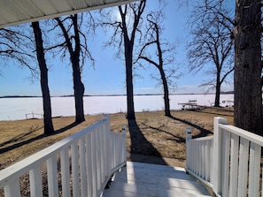 A wooden deck leading to a lake with trees and a picnic table.