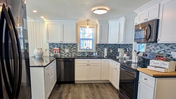 A modern kitchen with white cabinets, a black refrigerator, a microwave, and a wooden floor. - Lakefront Escape - Breathtaking Views in Fox Lake (Fox Lake)