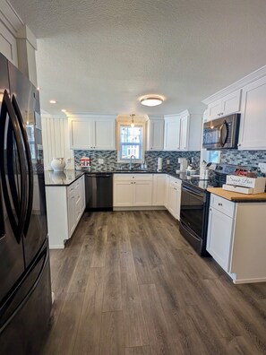 A modern kitchen with white cabinets, a black refrigerator, a microwave, and a wooden floor.