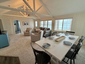 A spacious dining area with a high ceiling and large windows overlooking a body of water.