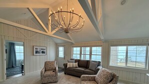 A spacious living room with a high ceiling, a chandelier, a large window with a view, and a patterned sofa. - Lakefront Escape - Breathtaking Views in Fox Lake (Fox Lake)