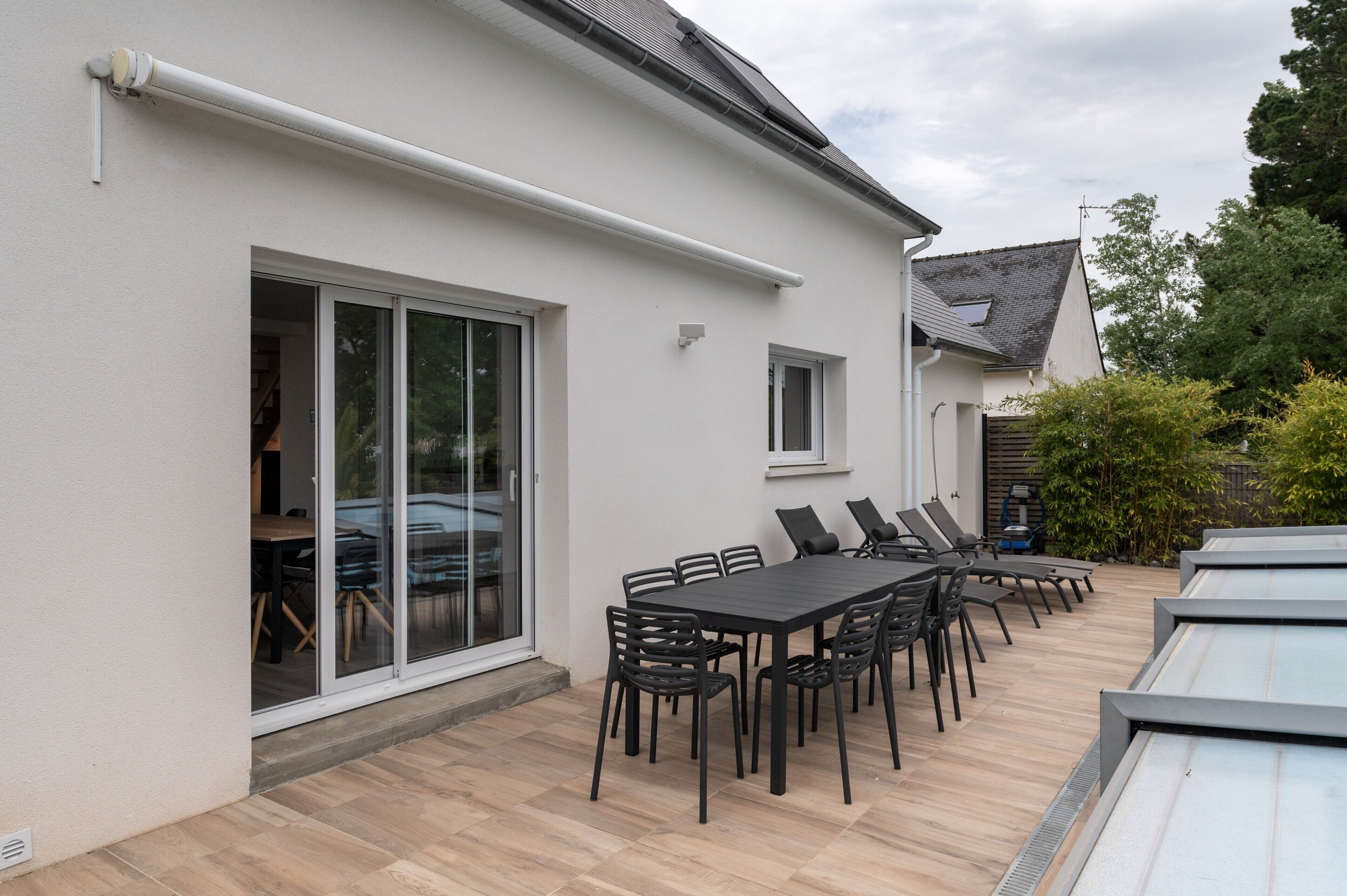 A modern house with a patio area featuring a dining table and chairs, a sliding glass door, and a small window.