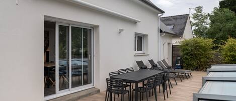 A modern house with a patio area featuring a dining table and chairs, a sliding glass door, and a small window.