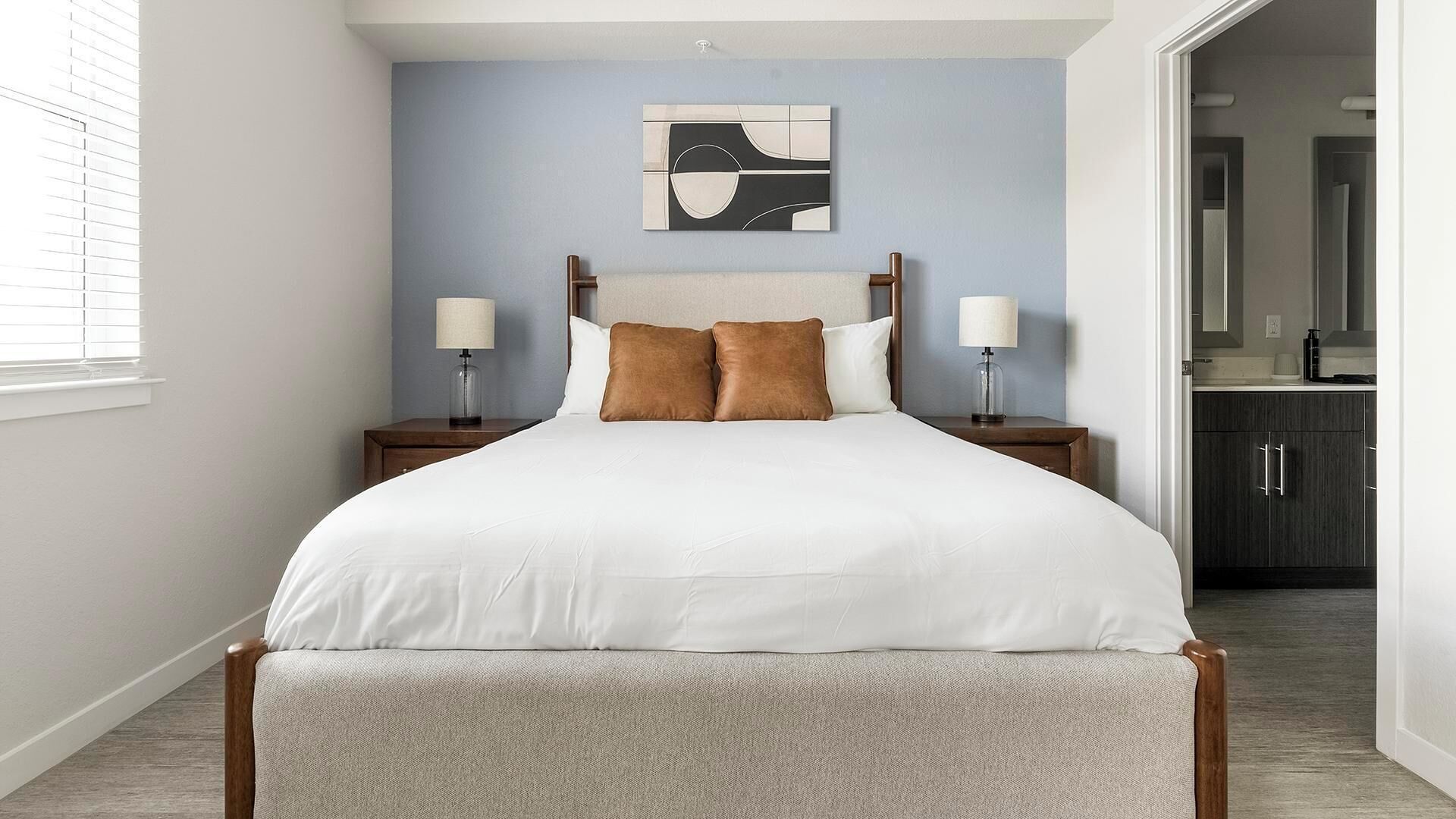 Une chambre à coucher comprenant un lit, deux tables de chevet, une commode, une œuvre d’art accrochée au mur et donnant sur la salle de bain.