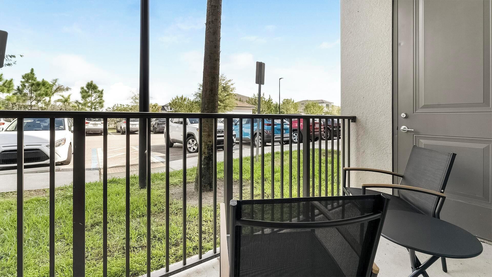 A balcony with a chair, a view of parked cars, and a building in the background.