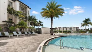 A hotel pool area with lounge chairs, palm trees, and a clear blue sky. - Landing | Stylish 1BD, Clubhouse, Gym (Fort Myers)