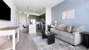 A modern living room with a grey sofa, black coffee table, and a TV. - Landing | Stylish 1BD, Clubhouse, Gym (Fort Myers)
