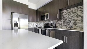 A modern kitchen with dark wood cabinets, stainless steel appliances, and a tiled backsplash. - Landing | Stylish 1BD, Clubhouse, Gym (Fort Myers)