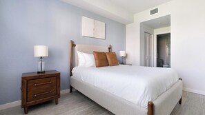 A bedroom with a bed, nightstands, a wooden dresser, and a door leading to a bathroom. - Landing | Stylish 1BD, Clubhouse, Gym (Fort Myers)