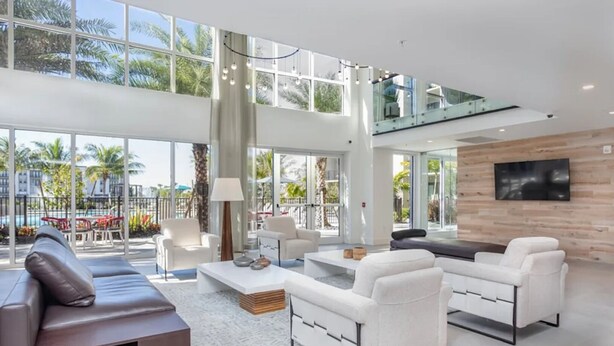 A spacious living area with a high ceiling, large windows, and a view of the outdoors. - Landing | Beautiful 1BD, Gym, Clubhouse (Fort Myers)