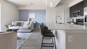 Eine moderne Küche mit einer zentralen Kochinsel, Barhocker und einem Essbereich mit einer Couch und einer Lampe.