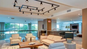 Un moderno vestíbulo de hotel con un sofá, sillas, una mesa de centro, un televisor y vistas al exterior.