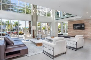 A spacious living area with a high ceiling, large windows, and a view of the outdoors. - Landing | Modern 1BD, Gym, Clubhouse (Fort Myers)