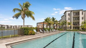 A swimming pool with lounge chairs and a palm tree, surrounded by apartment buildings. - Landing | Incredible 2BD, Gym, Clubhouse (Fort Myers)
