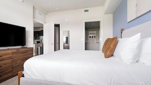 Ein Schlafzimmer mit Bett, Fernseher, Kommode und begehbarem Kleiderschrank.