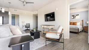 A modern living room with a sofa, a coffee table, a TV, a desk, and a chair. - Landing | Modern 2BD, Clubhouse, Gym (Fort Myers)