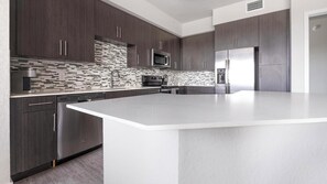 A modern kitchen with dark wood cabinets, a white countertop, stainless steel appliances, and a patterned backsplash. - Landing | Modern 2BD, Clubhouse, Gym (Fort Myers)