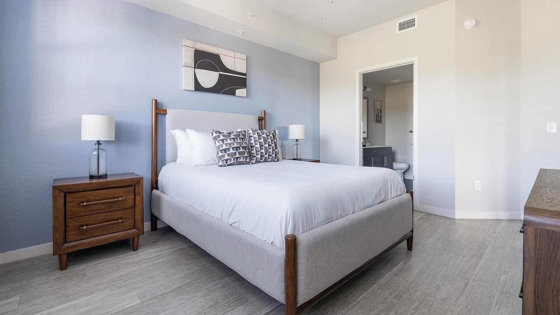 Une chambre à coucher comprenant un lit, des tables de chevet, une commode, un miroir et une porte donnant sur une autre pièce.