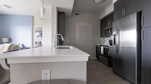 A modern kitchen with a central island, stainless steel appliances, and a view into the living area. - Landing | Chic 2BD, Clubhouse, Gym (Fort Myers)