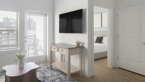 Een slaapkamer met een bed, een nachtkastje, een aan de muur bevestigde televisie en een raam met zonwering.