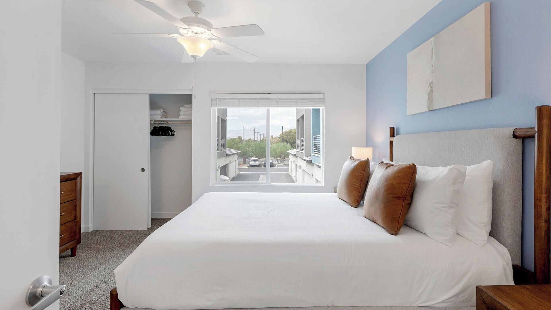 A bedroom with a bed, a ceiling fan, a window with a view, and a door leading to a closet.
