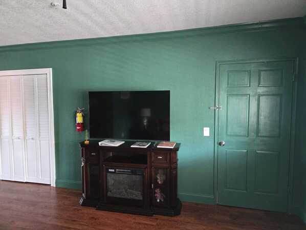 A room with a television on a stand, a door, and a fire extinguisher on the wall.