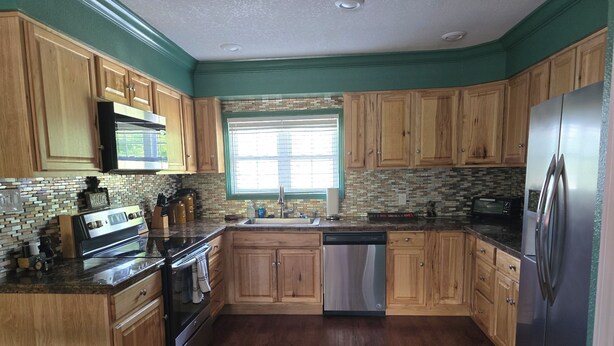 A kitchen with wooden cabinets, a stainless steel refrigerator, a dishwasher, and a window with blinds.