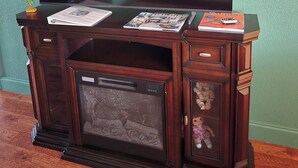 A wooden entertainment center with a flat-screen TV, magazines, and a fire extinguisher.