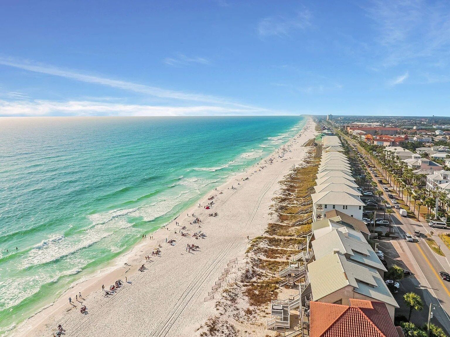 A coastal hotel with a beach view, a long row of rooms, and a clear sky.