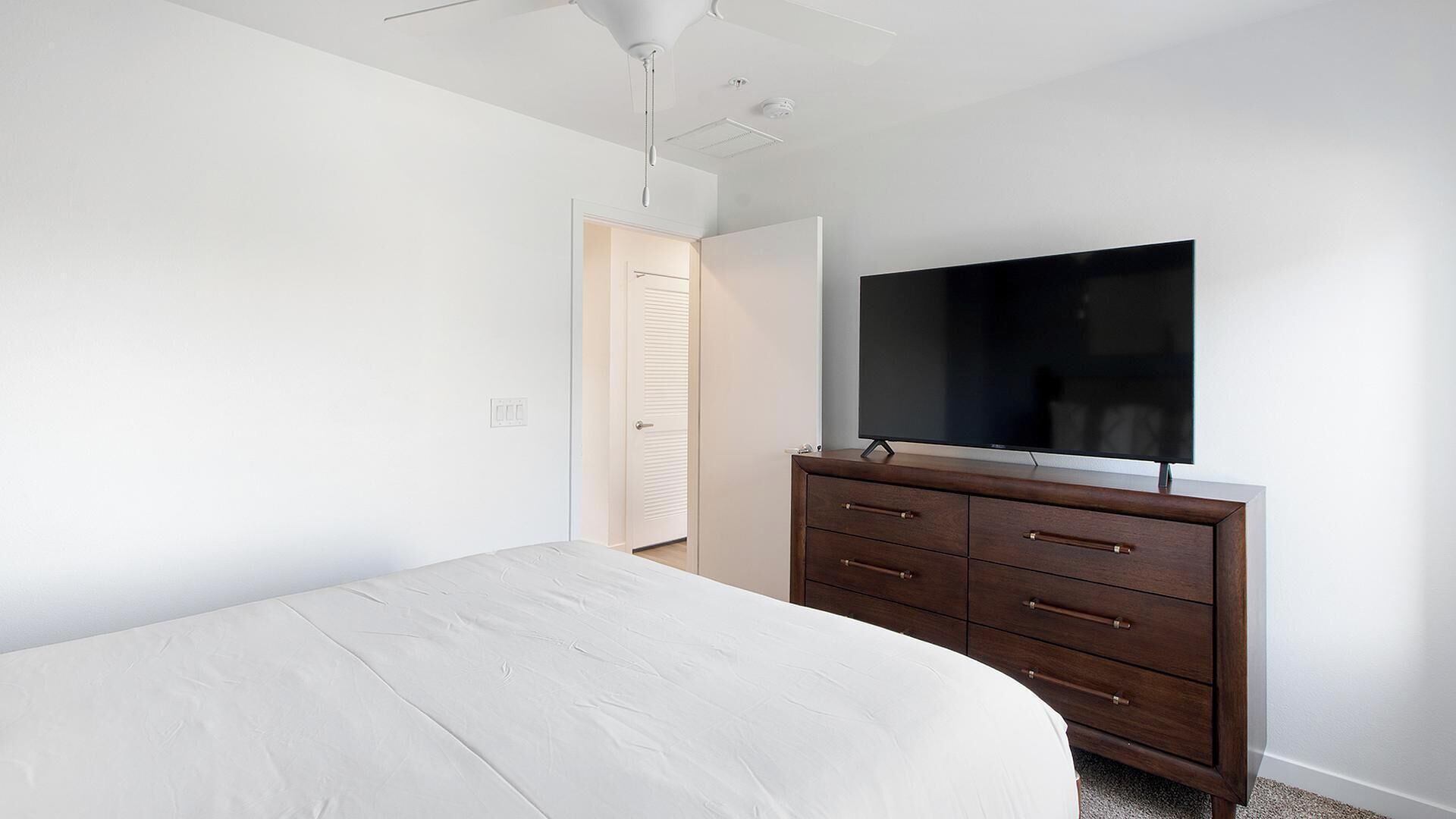 Una camera da letto con un letto, una cassettiera, una televisione e una porta.
