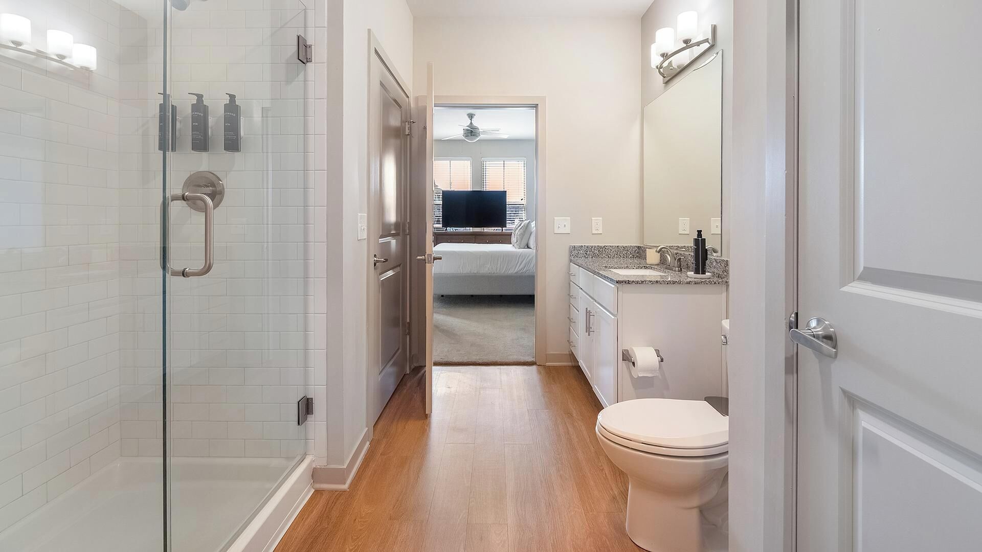 A modern bathroom with a glass shower enclosure, a toilet, and a sink with a granite countertop.