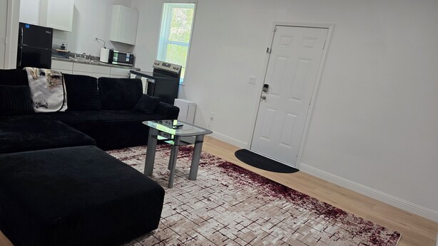 A living room with a black sofa, a glass coffee table, and a red and white patterned rug. - 2-bedroom building in charming Stockbridge with cool AC (Stockbridge)