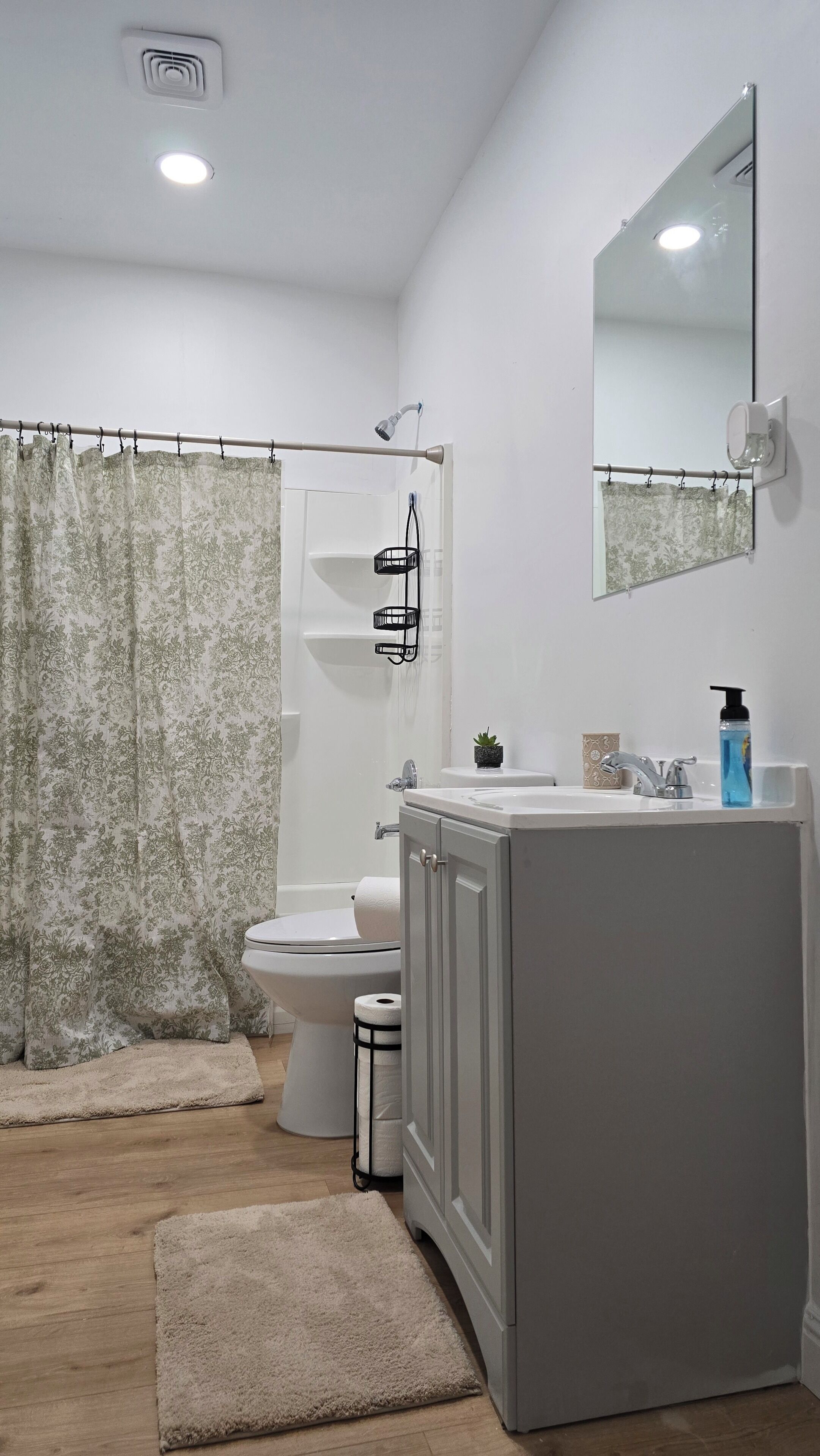 A bathroom with a toilet, shower, sink, and mirror.