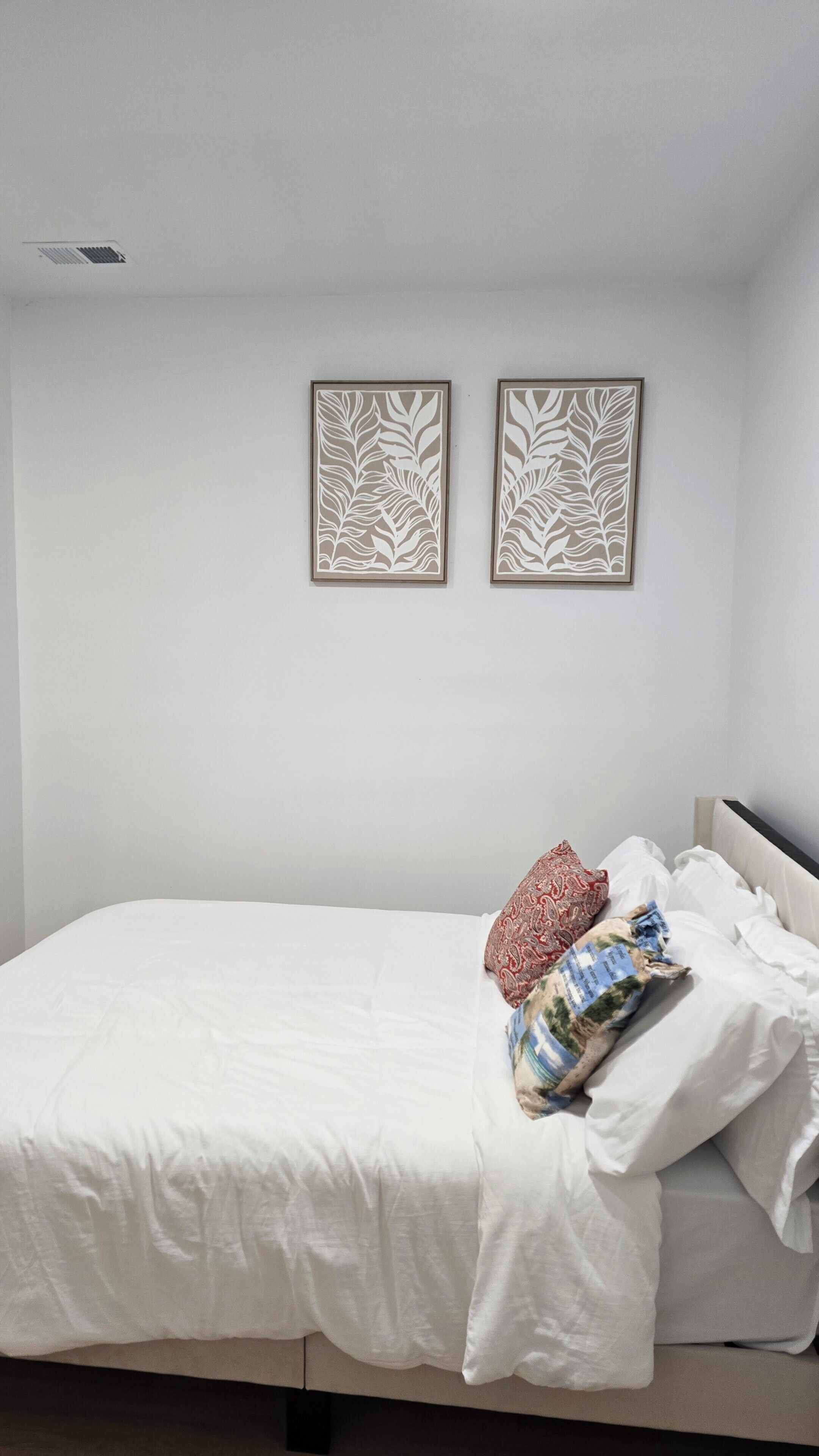 A bedroom with a bed, white bedding, two wall-mounted decorative panels, and a window.