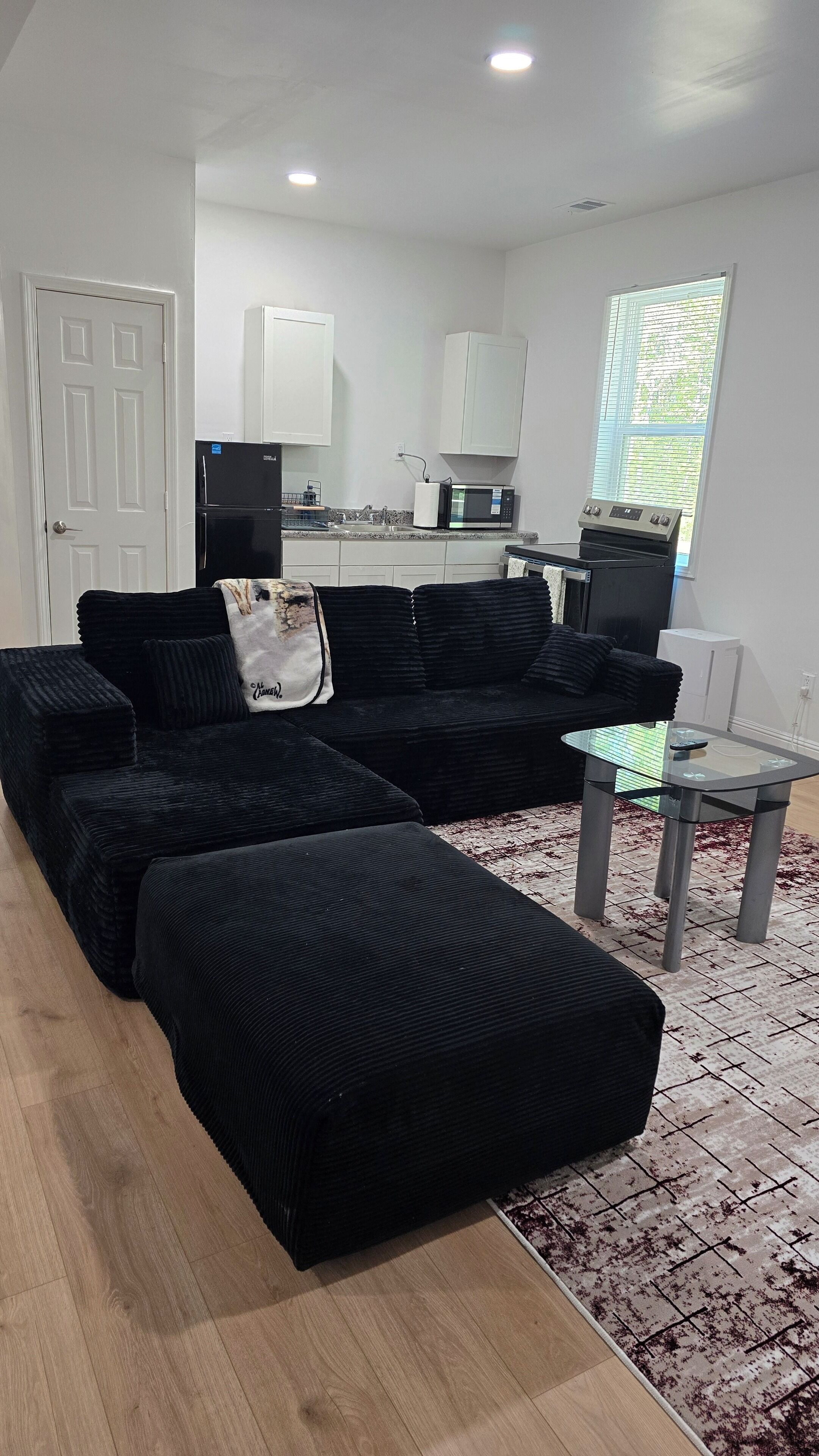 A modern living room with a sectional sofa, a glass coffee table, and a kitchen area with appliances.