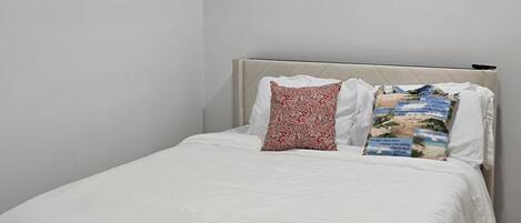 A bedroom with a bed, white bedding, two wall-mounted art pieces, and a ceiling light.
